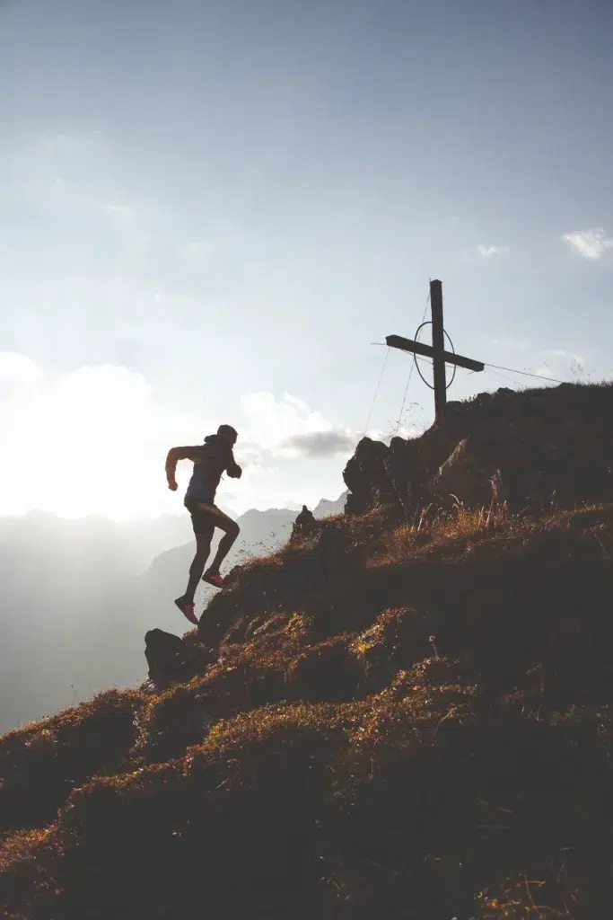 Eine Person genießt das Trailrunning im Ötztal und läuft bei Sonnenaufgang bergauf auf ein Holzkreuz zu.