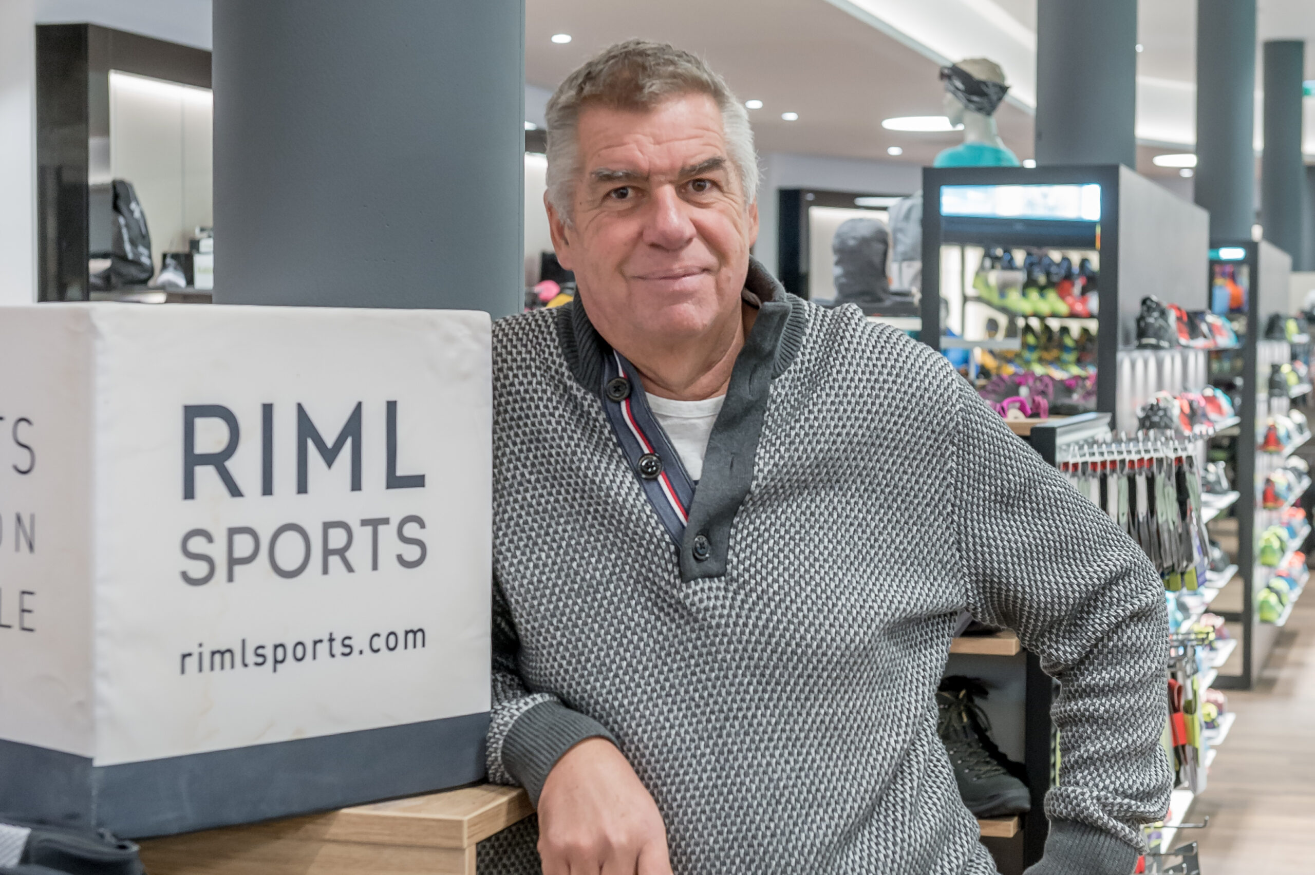 Mann in einem Sportgeschäft, der neben einer Auslage mit dem Zeichen RIML SPORTS steht.
