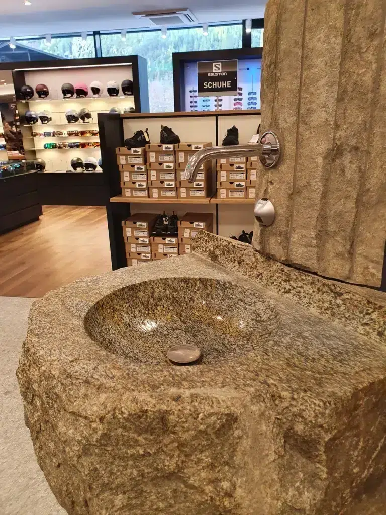 Ein Steinwaschbecken mit Metallhahn unterstreicht die Nachhaltigkeit im Sporthandel in diesem Schuh- und Helmgeschäft.