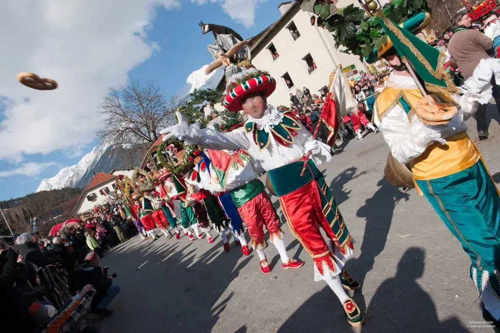 Menschen in bunten Kostümen werfen an der Fasnacht in Telfs während einer festlichen Bergparade Brezeln.
