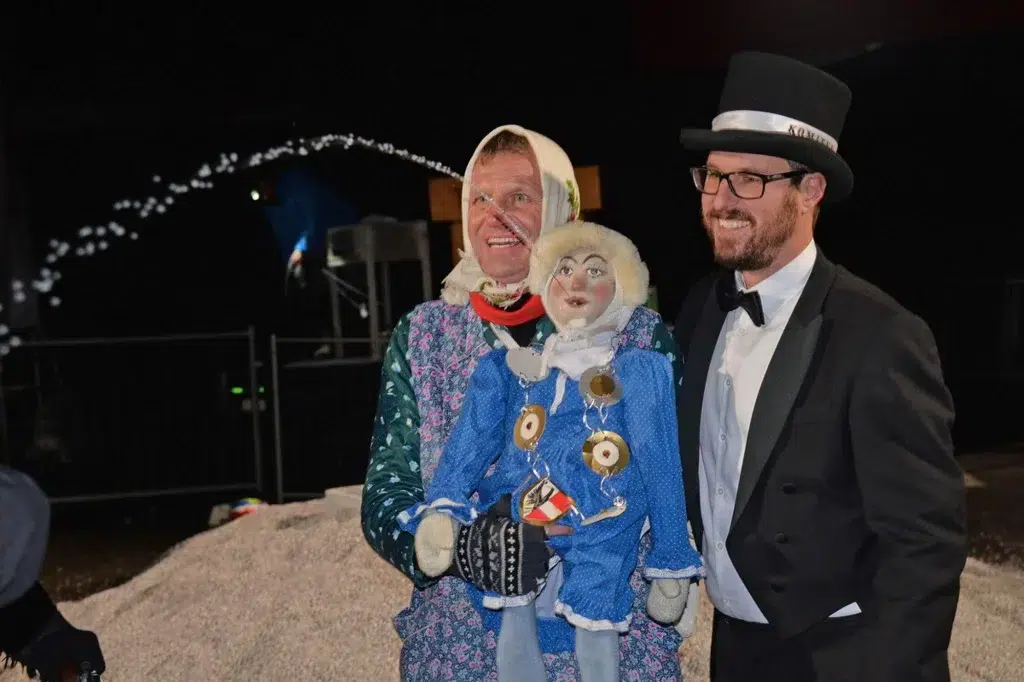 Zwei Männer posieren an der Fasnacht in Telfs, einer im Kostüm mit einer Puppe, der andere im Smoking.