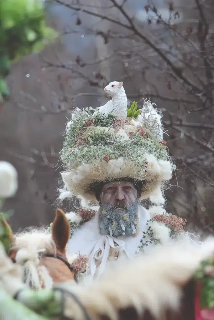 Person im Naturkostüm für die Fasnacht in Telfs, Hut mit weißer Tierfigur auf dem Kopf.