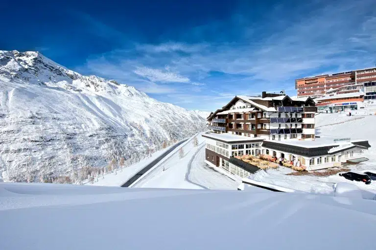 Ein verschneites Bergdorf mit dem Hotel Angerer Alm und dem klaren blauen Himmel im Hintergrund.