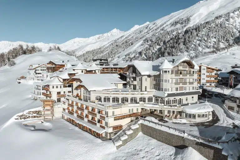 Hotel Alpenaussicht: Großer alpiner Hotelkomplex, eingebettet zwischen verschneiten Bergen und Kiefern.