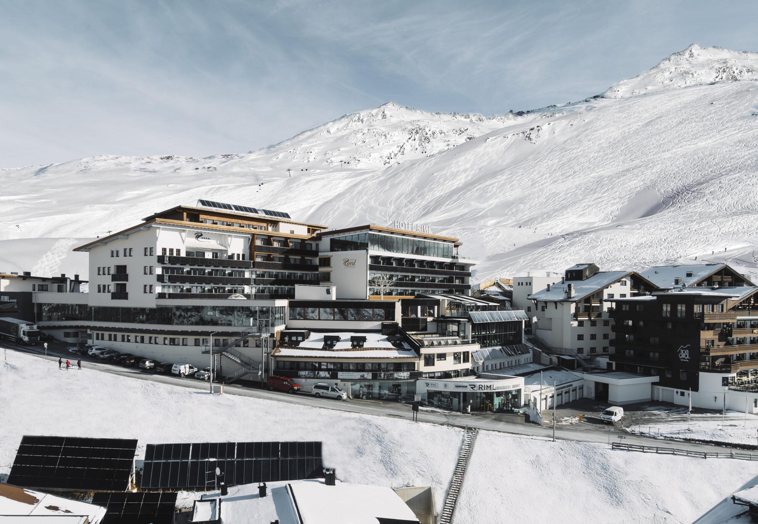 Modern alpine hotel complex nestled in snowy mountains under a clear blue sky.