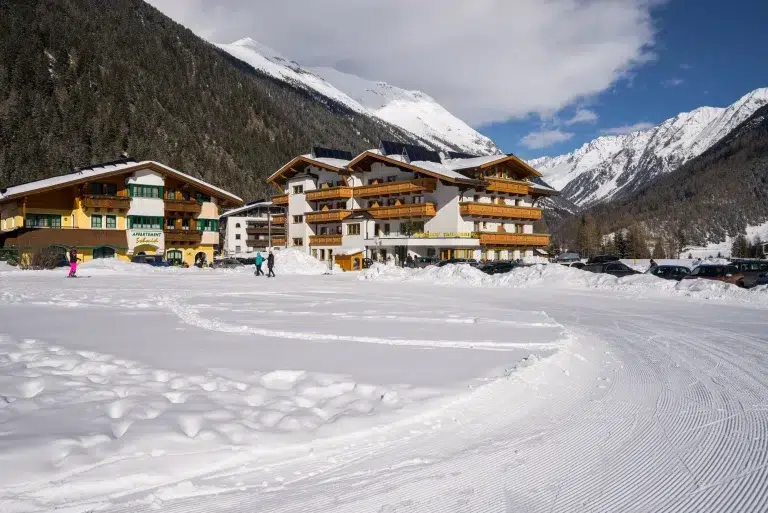 Verschneites Alpendorf mit Gebäuden im Chalet-Stil und Bergen im Hintergrund.