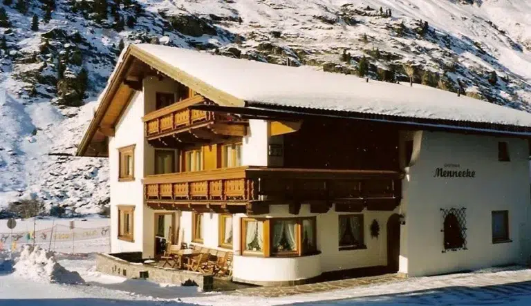 Haus Mennecke im Chalet-Stil mit schneebedecktem Dach in einer verschneiten Berglandschaft.