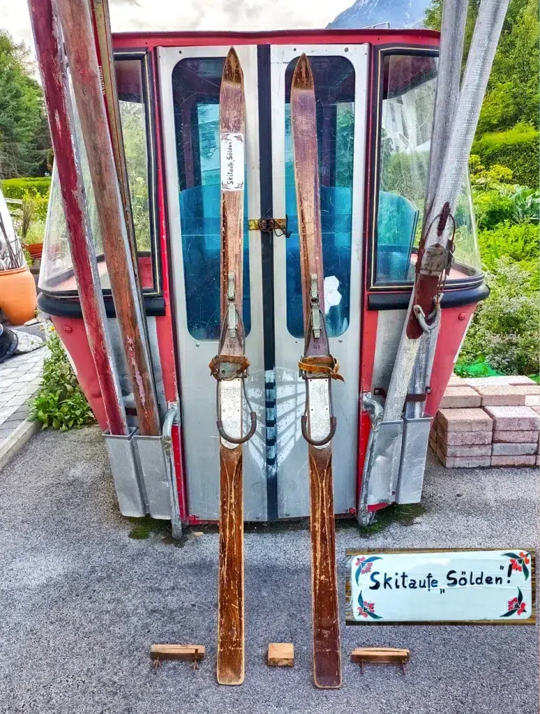 Zwei Paar alte Holzskier warten vor einer roten Gondel - perfekt für ein Skiinfluencer-Foto.