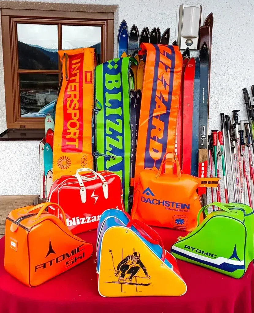 Farbenfrohe Vintage-Skisäcke und Skier bilden ein Skiinfluencer-würdiges Bild an der Wand.