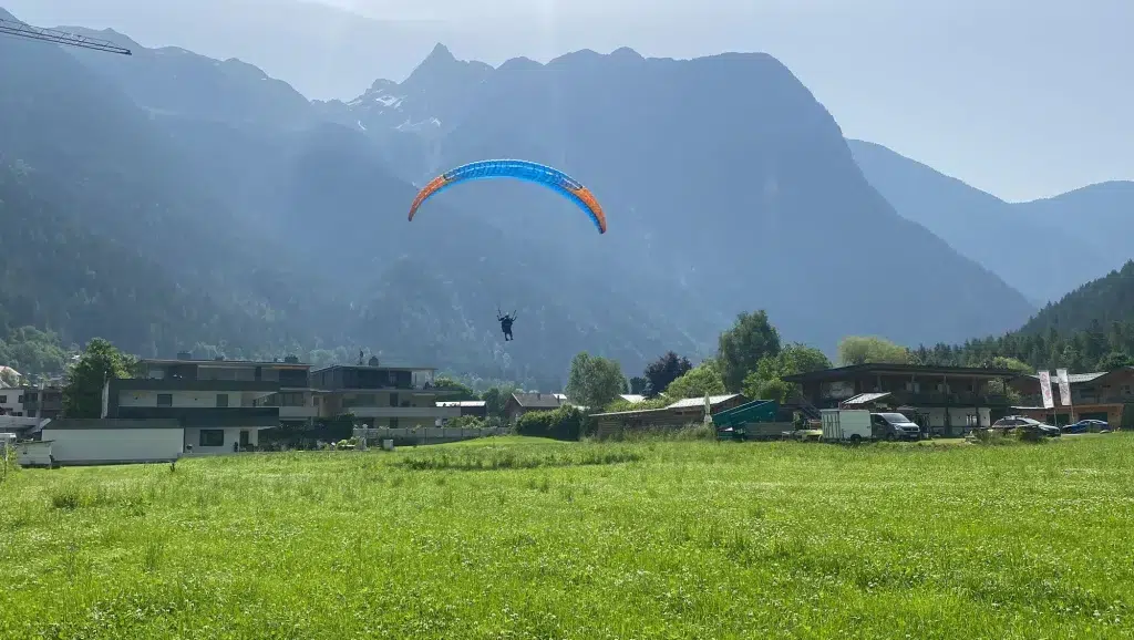 Eine Person, die einen Fly Airea Tandem-Gleitschirmflug über einer Wiese und den Bergen genießt.