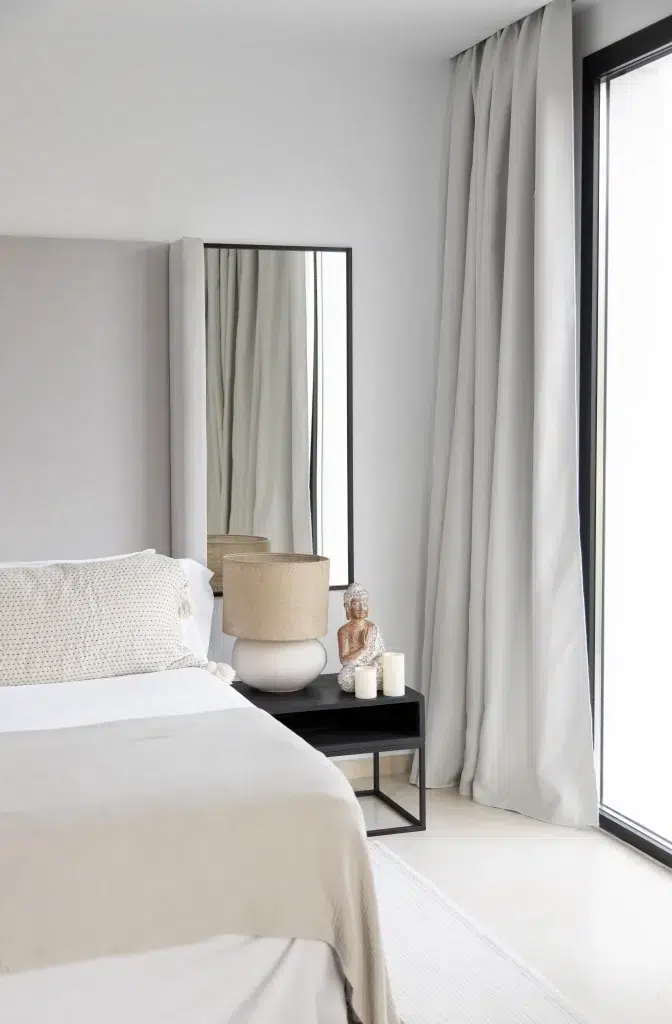 Minimalistisches Schlafzimmer mit neutralen Tönen von Snow Society, Bett, Beistelltisch, Lampe und Statue am Fenster.