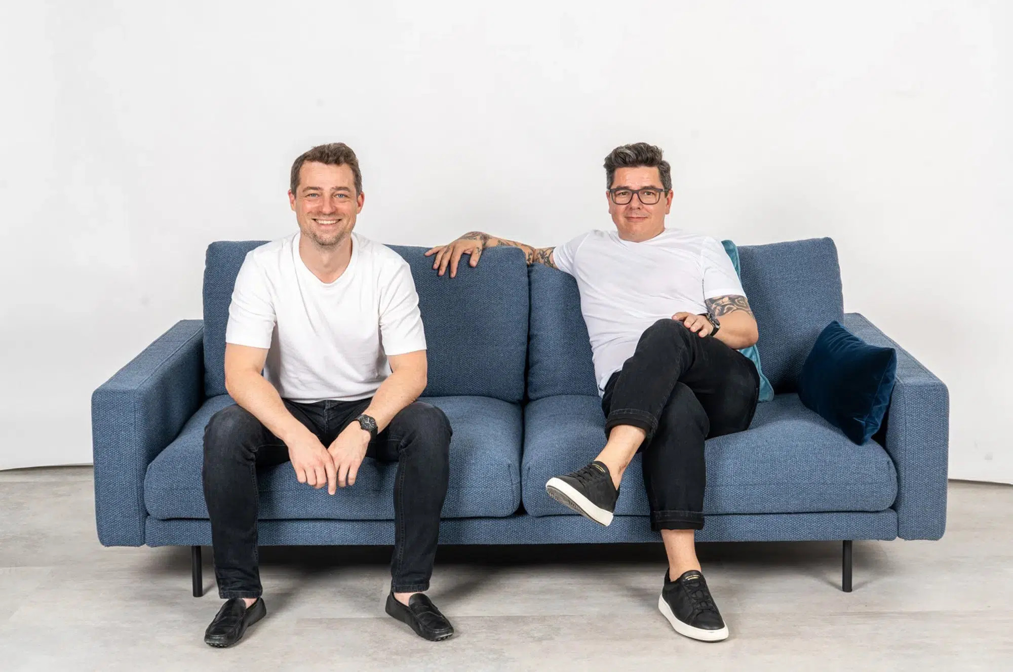 Zwei Personen in Freizeitkleidung auf einem blauen Sofa vom Einrichtungshaus Föger, die in die Kamera lächeln.