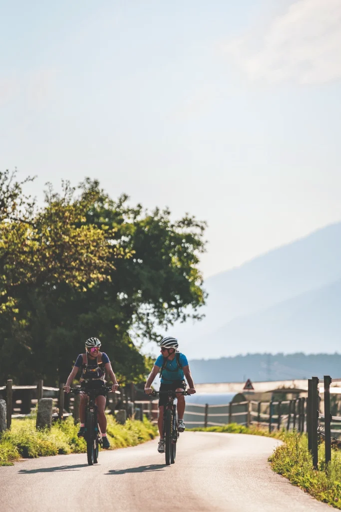 Zwei Radfahrer genießen eine sonnige Landstraße, die die Vorzüge des Fahrrad-Leasings in der Natur hervorhebt.