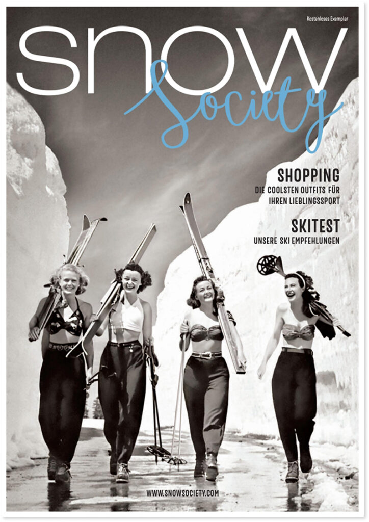 Vier lächelnde Frauen in alten Skikostümen gehen mit Skiern spazieren - ein echter Snow Society-Moment.