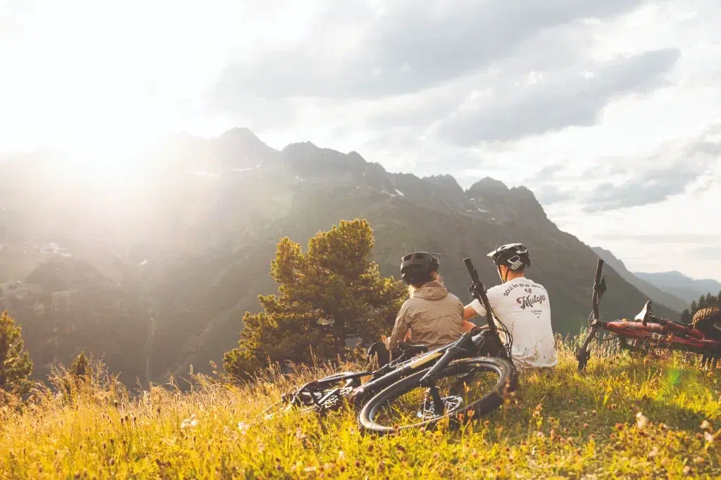 Zwei Radfahrer entspannen sich auf einer Wiese mit ihren Rädern und genießen die Berge - entdecken Sie Bike Leasing.