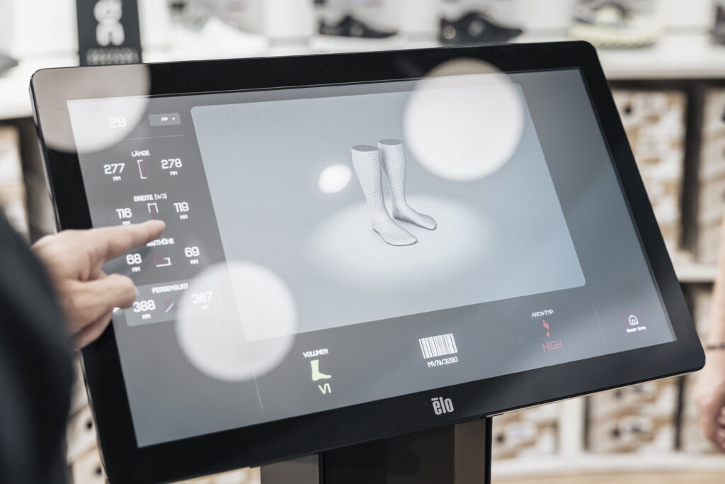 Ein Touchscreen zeigt ein 3D-Modell von Stiefeln mit Daten zur Schuhanpassung für Sicherheit am Berg.