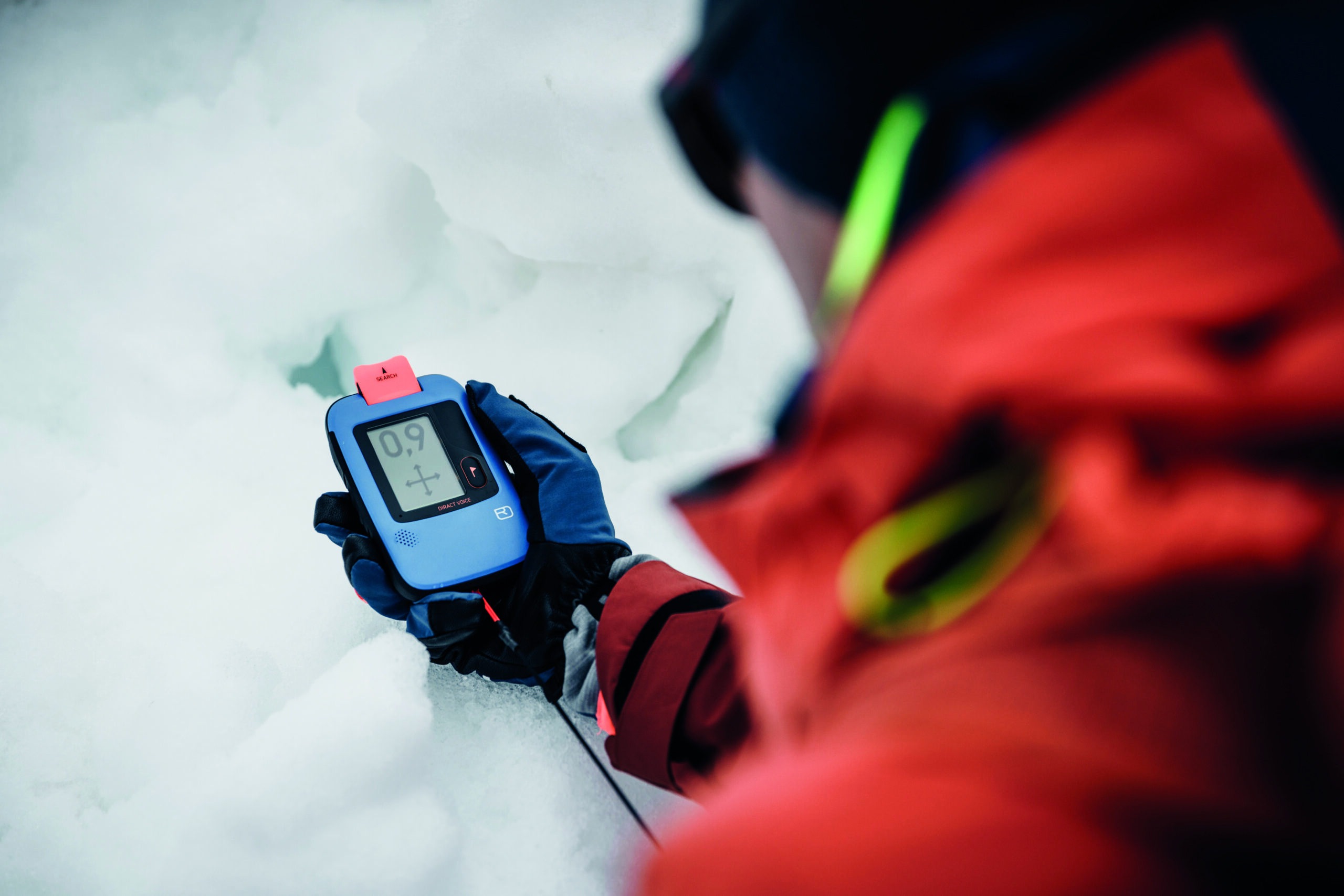 Eine Person in roter Jacke aus der Ethnie hält ein digitales Gerät, das 0,9 anzeigt, in den Schnee.